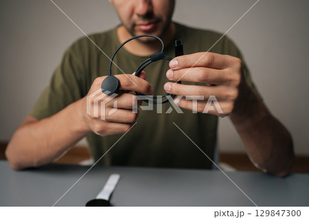 Cropped shot of male hands holding smartwatch inductive charger, preparing to power up smart watch, sitting at table on isolated background. Concept of healthy lifestyle. Cropped shot of male hands holding smartwatch inductive charger, preparing to power up smart watch, sitting at table on isolated background. Concept of healthy lifestyle. 129847300