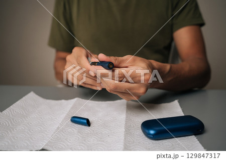 Man cleaning electronic cigarette emphasizing importance of hygiene and maintenance in vaping sitting at table with on white paper towel. Process of maintaining heated electronic cigarette device. 129847317