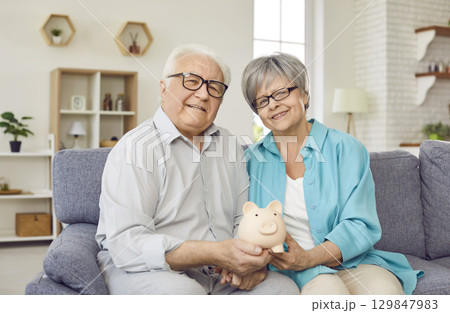 Portrait of happy senior married couple saving their family budget and saving for future. 129847983
