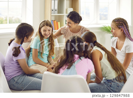 School psychologist woman having conversation with group of children girls sitting in a circle. 129847988