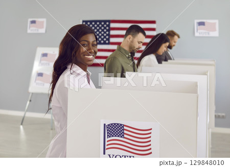 Happy american voter woman putting her ballot in bin on election day standing at vote center. Happy american voter woman putting her ballot in bin on election day standing at vote center. 129848010