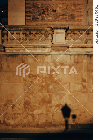 A moody vertical image of a stone wall with a decorative railing and a lamppost shadow. A stone wall with a decorative railing and the shadow of a lamppost, bathed in warm light. Abstract street shot. 129850461