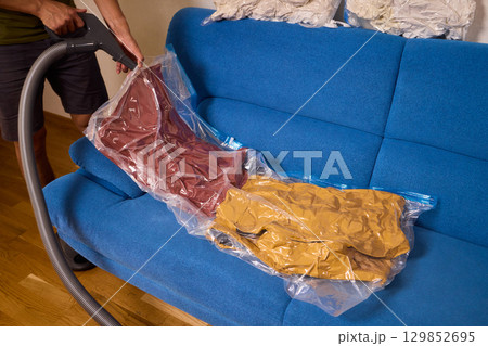 A man on a cozy blue couch uses a vacuum sealer to pack his clothes, enjoying a relaxing day A man on a cozy blue couch uses a vacuum sealer to pack his clothes, enjoying a relaxing day 129852695