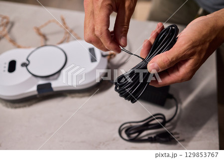 Hands Skillfully Organizing a Charging Cable Neatly in Proximity to a Device Across the Table 129853767