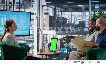 Diverse management group does strategic thinking next to chroma key, analyzing data to guide company decisions with research. Reviewing performance metrics and multicultural perspectives. Camera B. 129854005