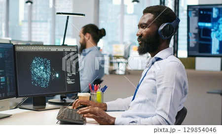 Software developer testing generative AI machine learning algorithms and listening music at work. African american man wearing headphones scaling productivity with AI large language model, camera A 129854046