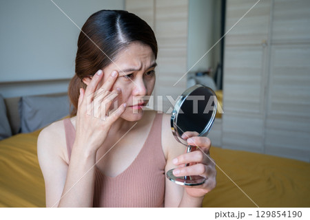 Asian woman worried about her face when she saw acne and wrinkled occur on her face by mini mirror. Allergies, irritants, genetic makeup, etc can cause skin conditions. 129854190