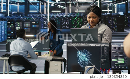 Annoyed data center admin having trouble doing node tree programming. Irked woman in server room having glitching issues while using predictive AI visualization systems on notebook, camera A 129854220