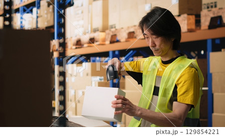 Asian employee scanning shipping labels and barcodes on packages, manages labeling registration with a scanner and handling inventory tracking. E-commerce fulfillment center. Camera B. 129854221