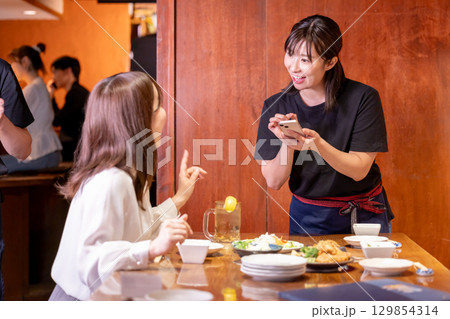 居酒屋　スマホで注文をとる女性スタッフ 129854314