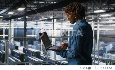 Data center software developer panicking after receiving critical error popup on laptop display. African american woman in server hub alerted by bugs causing low hardware performance Data center software developer panicking after receiving critical error popup on laptop display. African american woman in server hub alerted by bugs causing low hardware performance 129854328