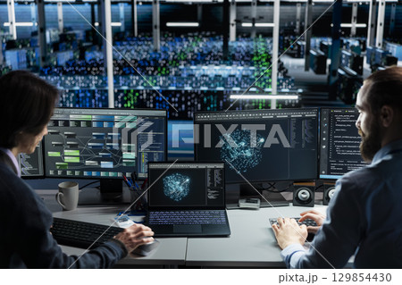 Data center technicians monitoring AI applications, adjusting machine learning parameters. Teamworking server hub workers collaborating, enhancing artificial intelligence software performance 129854430