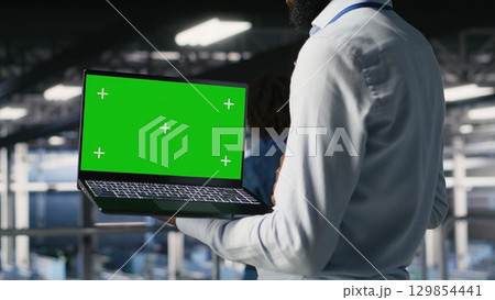 Close up of engineer on data center industrial platform analyzing performance outputs on green screen laptop. Server room IT expert finetuning server rig configurations using mockup notebook 129854441
