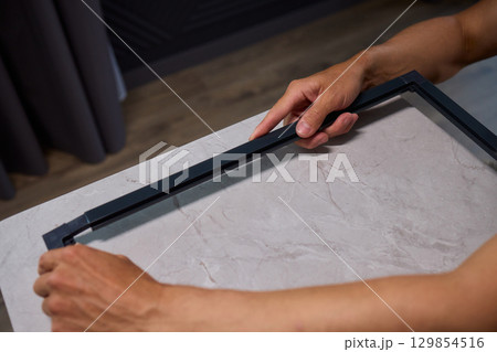 Hand Assembling a Frame on a Beautiful and Modern Table in a Creative Workspace 129854516