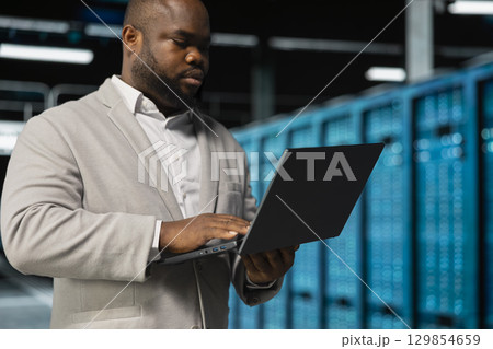 Software developer in server farm managing infrastructure systems, checking recovery plan. Data center IT specialist monitoring performance using notebook, making sure rigs are functioning optimally 129854659