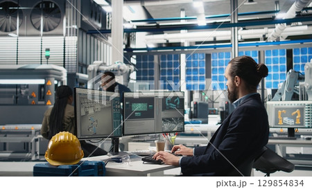 Professional inspector reviewing manufacturing process data on computer, ensuring seamless solar panels production in the photovoltaics factory. Expert works on renewable energy. Camera A. 129854834