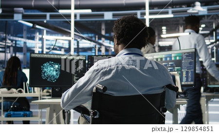 Server room programmer with paraplegia interprets AI generated data analytics graphs. Man in wheelchair using artificial intelligence program showing predictive system metrics in data center, camera A Server room programmer with paraplegia interprets AI generated data analytics graphs. Man in wheelchair using artificial intelligence program showing predictive system metrics in data center, camera A 129854851