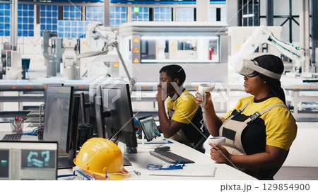 Photovoltaics factory technician using VR headset to assembly digital solar cells, placing solar panels via robot arms. Woman expert inspecting solar plant machinery using virtual reality. Camera B. Photovoltaics factory technician using VR headset to assembly digital solar cells, placing solar panels via robot arms. Woman expert inspecting solar plant machinery using virtual reality. Camera B. 129854900