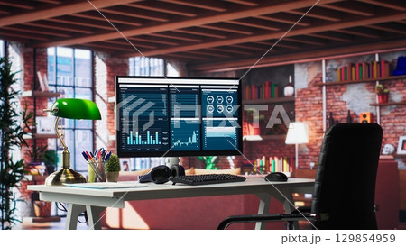 Modern home office with desktop PC monitor displaying business analytics and marketing infographics, clean minimalist desk setup. Bright stylish loft offers a trendy professional ambiance. Modern home office with desktop PC monitor displaying business analytics and marketing infographics, clean minimalist desk setup. Bright stylish loft offers a trendy professional ambiance. 129854959