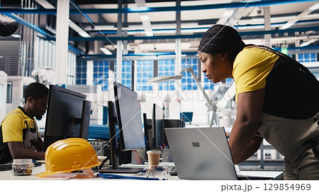 Photovoltaics factory technician designing CAD models and technical sketches for solar modules on laptop. Woman engineer ensures solar panel designs for efficiency and manufacturability. Camera B. 129854969