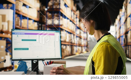 Industrial worker in hi vis vest placing shipping labels and scanning awb barcode for package tracking software registration. Asian man ensures merchandise labeling before delivery. Camera A. Industrial worker in hi vis vest placing shipping labels and scanning awb barcode for package tracking software registration. Asian man ensures merchandise labeling before delivery. Camera A. 129855005