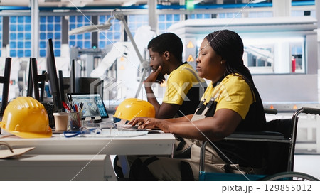 Woman with disability works in photovoltaics factory on designing solar cells, debugging and fixing malfunctioning systems. Plant worker wheelchair user ensuring operational reliability. Camera A. 129855012