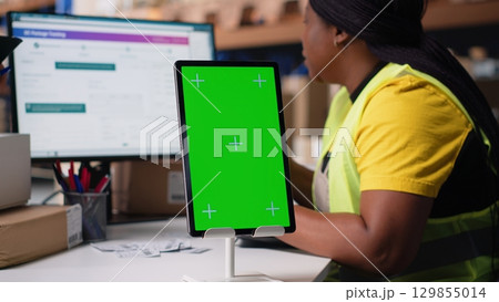 Employee reviews copy space monitor in the storage room for data entry, inventory tracking mockups and visuals or barcode printer interfaces. Distribution hub staff manages cargo. Camera B. 129855014