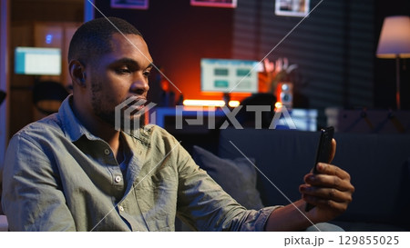African american guy attends web conference call on laptop sitting at home, joining an remote webinar to discuss about solving daily tasks. Teleconference in the living room. Camera A. African american guy attends web conference call on laptop sitting at home, joining an remote webinar to discuss about solving daily tasks. Teleconference in the living room. Camera A. 129855025