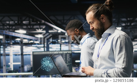 Technician holding laptop walking on server farm platform, doing AI machine learning automatization. Data center programmer using notebook, doing maintenance using artificial intelligence Technician holding laptop walking on server farm platform, doing AI machine learning automatization. Data center programmer using notebook, doing maintenance using artificial intelligence 129855186