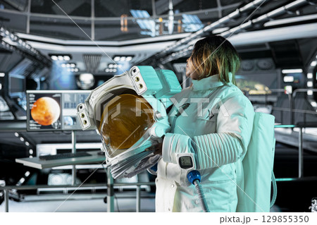 Astronaut holds helmet in orbital station, analyzing Mars planetary data on digital monitors. Crew member observes Martian surface research to assist future planetary exploration and mission planning 129855350