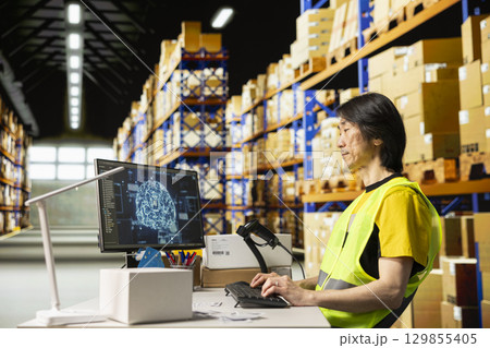 Asian warehouse clerk using AI brain systems with neural networks, using virtual assistant to process orders and ensure express delivery. Updating the tracking software on computer. 129855405