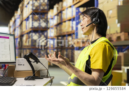 Asian employee answering calls from clients in a distribution hub, handling mix up problems and requests via customer service. Call center clerk troubleshooting parcel shipment. Logistics. Asian employee answering calls from clients in a distribution hub, handling mix up problems and requests via customer service. Call center clerk troubleshooting parcel shipment. Logistics. 129855584
