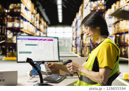 Asian male worker scanning shipment labels and tracking numbers in a distribution hub, ensures order management in fulfillment center. Using a scanner for transportation details. 129855594