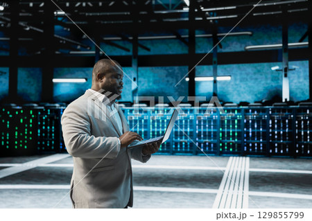 Developer in data center updating systems using laptop, protecting mainframes from damaging software errors. Server hub IT expert using notebook, looking for malfunctions causing gear to slow down 129855799