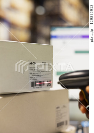 Close up of staff member managing barcodes awb scanning tasks for online shopping orders, products with shipping labels and details for easy delivery. Fulfillment center employee. 129855912