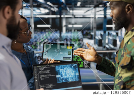 Military technicians in secure data center monitoring AI tech systems. Black army operator in server hub ensuring stable infrastructure for machine learning defense operations. Military technicians in secure data center monitoring AI tech systems. Black army operator in server hub ensuring stable infrastructure for machine learning defense operations. 129856007