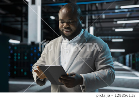 Engineer in server farm coordinating backups protocols, checking recovery plan. Data center IT specialist performing maintenance with tablet, making sure rigs are functioning optimally Engineer in server farm coordinating backups protocols, checking recovery plan. Data center IT specialist performing maintenance with tablet, making sure rigs are functioning optimally 129856118
