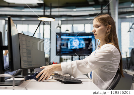 Junior dev speeding up tasks by following AI language model suggestions in office. Young woman relying on artificial intelligence LLM assistant to fix mistakes during startup internship 129856202