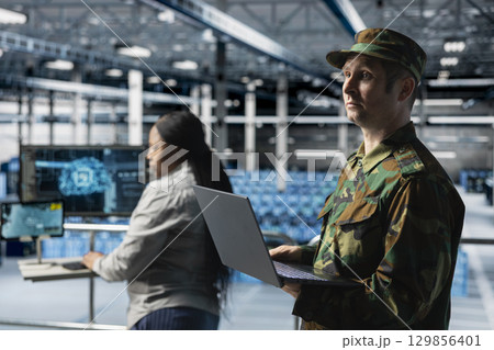 Data center army specialists configuring rigs to support AI integration in military infrastructure. Military server room colleagues enabling autonomous defense operations using AI 129856401