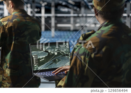 Close up of army specialist in data center scanning terrain after enemy lines using military satellite control. Soldier wearing uniform in server room managing orbital telemetry on notebook Close up of army specialist in data center scanning terrain after enemy lines using military satellite control. Soldier wearing uniform in server room managing orbital telemetry on notebook 129856494