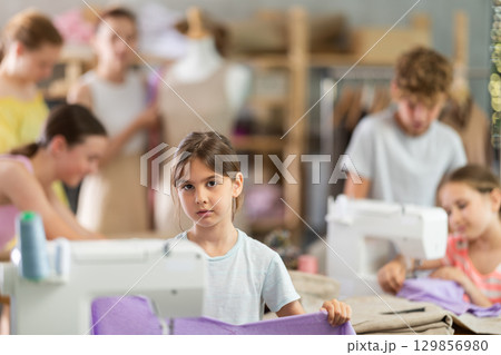Little girl checking stitched fabric at school sewing workshop 129856980