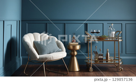 Luxurious modern interior design shows comfortable armchair beside striking blue wall. Elegant gold furniture, including stylish bar cart, decorates chic room, providing sophisticated and inviting Luxurious modern interior design shows comfortable armchair beside striking blue wall. Elegant gold furniture, including stylish bar cart, decorates chic room, providing sophisticated and inviting 129857136