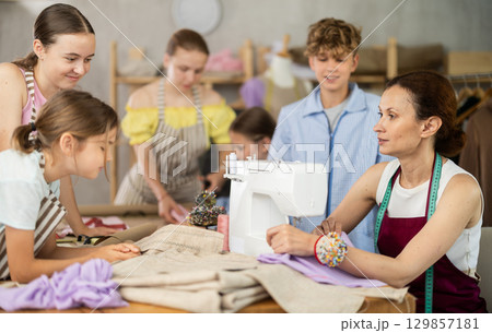 School-age students learning sewing from female instructor in tailoring workshop 129857181