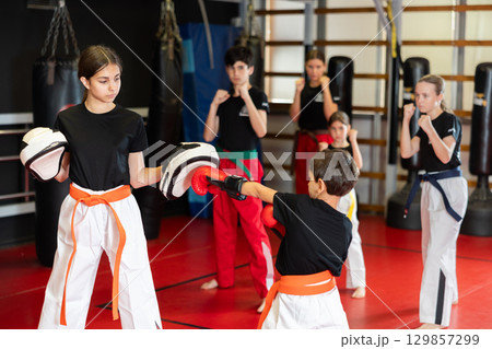 Teenage girl in boxing mitts trains with boy in boxing gloves Teenage girl in boxing mitts trains with boy in boxing gloves 129857299