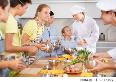 Interested teenage girl talking to chef and children at group culinary class Interested teenage girl talking to chef and children at group culinary class 129857395