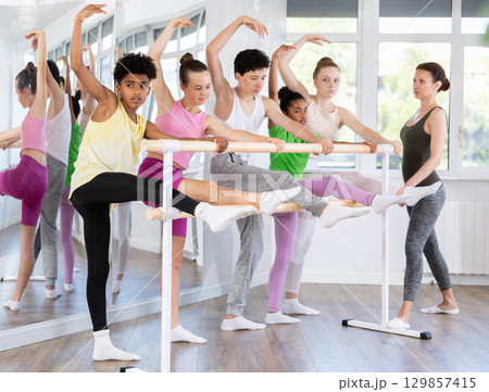 Teenage boy doing leg stretching exercise holding by ballet barre during dance courses 129857415