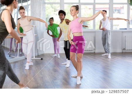 Positive teenage girl practicing ballet positions standing in row with others Positive teenage girl practicing ballet positions standing in row with others 129857507