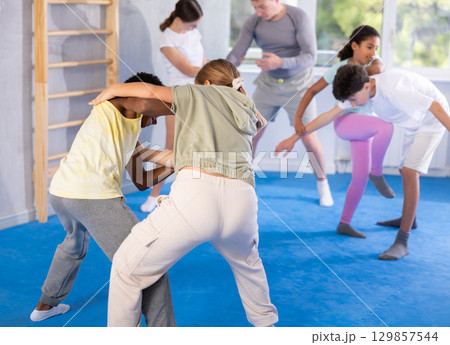 Girls and boys practicing in pair self defence movements with male trainer supervision 129857544
