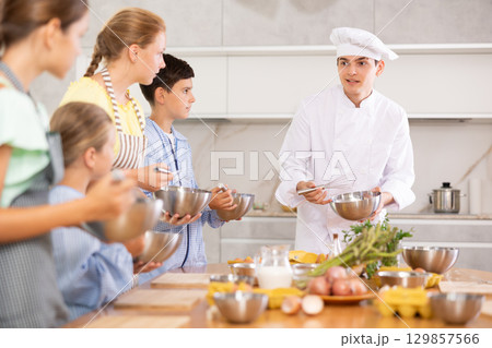 Cooking class, culinary, food and people concept - happy group of children and male chef cook cooking in modern kitchen Cooking class, culinary, food and people concept - happy group of children and male chef cook cooking in modern kitchen 129857566