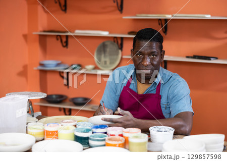 Man ceramist painting new crafted plate Man ceramist painting new crafted plate 129857598